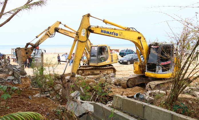 Sattahip Naval Base use backhoes and tractors to tear down a wall near the beach at the Ton Had Restaurant and Resort.