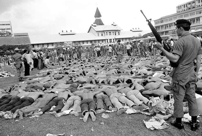 Police stand guard over leftist Thai students on a soccer field at Thammasat University. (AP Photo/Neal Ulevich, Oct. 6, 1976 File)