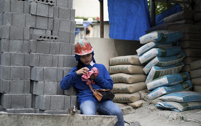 A Cambodian migrant construction worker checks her phone outside a building site in downtown Bangkok. The large numbers of women migrant construction workers in Thailand only serve to magnify their problems, including lower pay and the risk of being fired if they get pregnant. (AP Photo/Dake Kang)