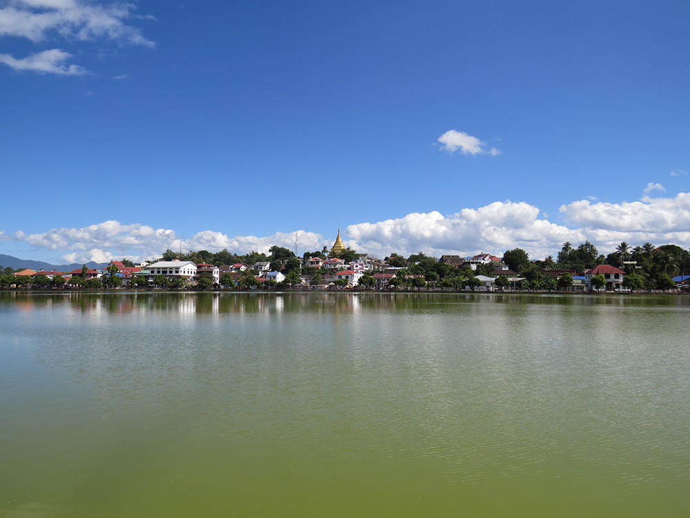 The scenic Naung Tong Lake in Kengtung, Myanmar is capped by the golden glow of Wat Jom Kai.