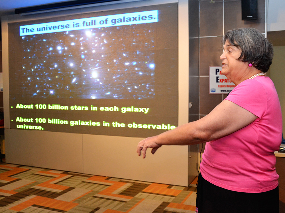 Alicia Beaudin explains to her PCEC audience that Cosmology includes our universe, which is full of galaxies. She points out that there are about 100 billion stars in each galaxy and 100 billion galaxies in the observable universe.