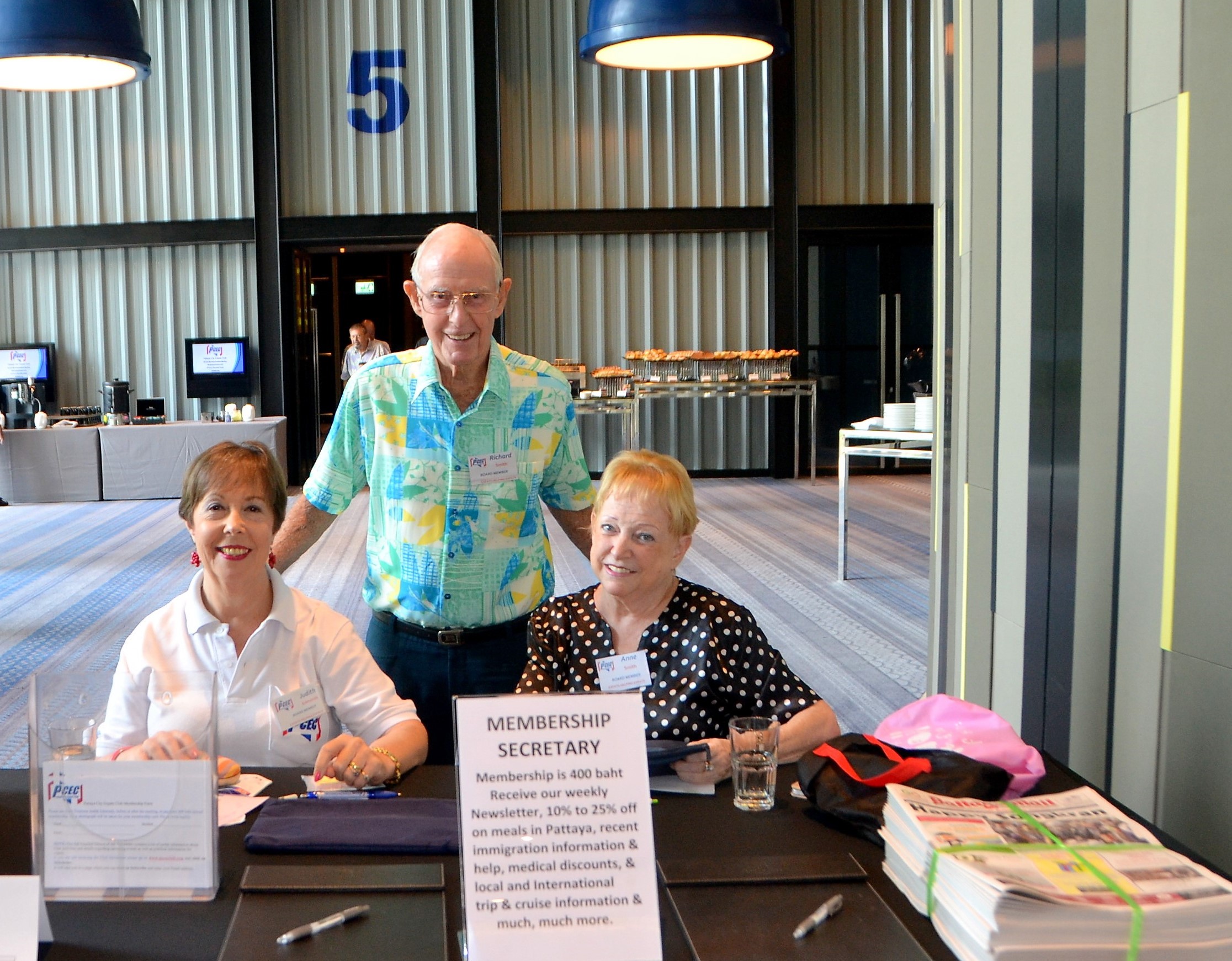 Judith Edmonds with the able assistance of Anne Smith are on hand to take membership applications before the PCEC Sunday meeting program starts. Here they pose for the camera with Vice Chairman Richard Smith; also, on the desk are copies of the Pattaya Mail available free for members and guests.