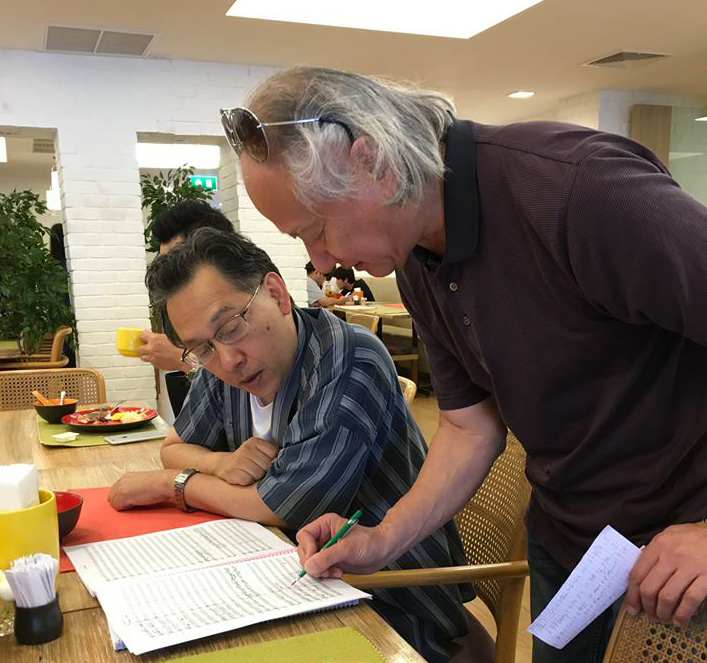 Composer Narongrit Dhamabutra (left) and conductor Hikotaro Yazaki discuss a point in the Sinfonia Chakri score.