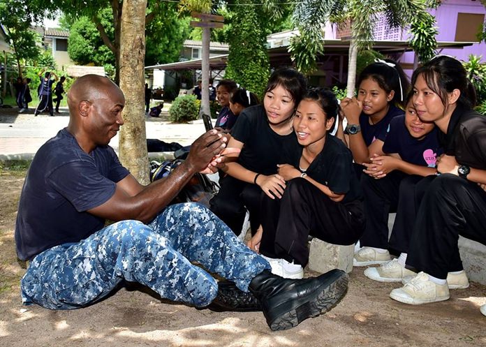 Capt. Alexis Walker, Deputy Commander, Destroyer Squadron 7, uses an app on his cellular phone to communicate with children from Banntunggard School.