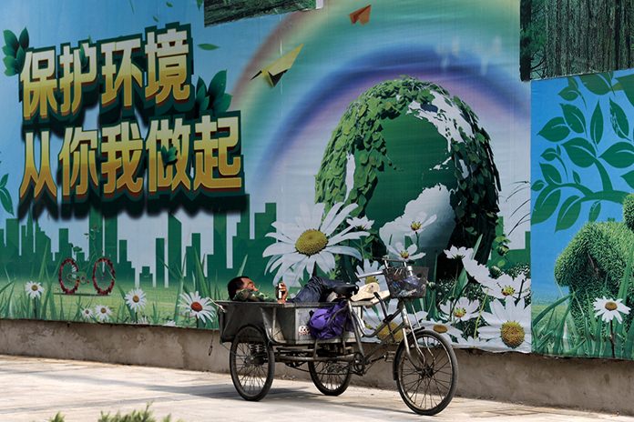 A migrant worker listens to radio parked next to a billboard promoting environment protection with the slogan “Environment protection starts from you and me” on display in Beijing. U.S. President Donald Trump said the United States “will continue to be the cleanest and most environmentally friendly country on Earth”. But facts muddy that claim. (AP Photo/Andy Wong)