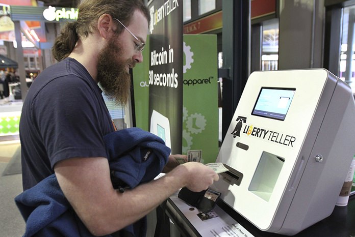 In this Monday, March 31, 2014, file photo, Tim McCormack, of Boston, inserts cash into a Liberty Teller ATM while purchasing bitcoins at South Station train station, in Boston. On Thursday, Sept. 14, 2017, Bitcoin tumbled 15 percent to about $3,300 against the dollar. (AP Photo/Steven Senne, File)