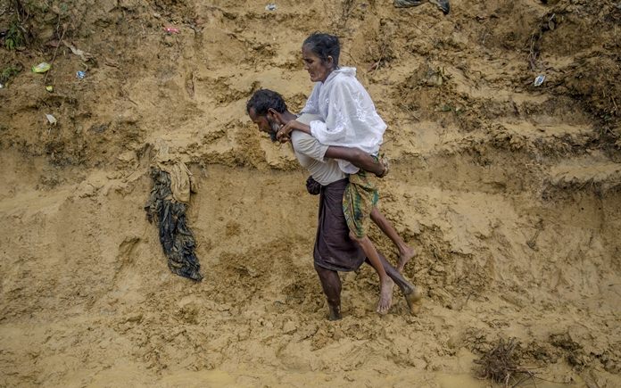 In this Thursday, Sept. 21, 2017 file photo, Alishaan, a Rohingya Muslim man, carries his sick mother Aishya Khatoon to a hospital at Taiy Khali refugee camp, Bangladesh. More than 400,000 Rohingya Muslims have fled to Bangladesh since Aug. 25, when deadly attacks by a Rohingya insurgent group on police posts prompted Myanmar’s military to launch “clearance operations” in Rakhine state. (AP Photo/Dar Yasin, File)