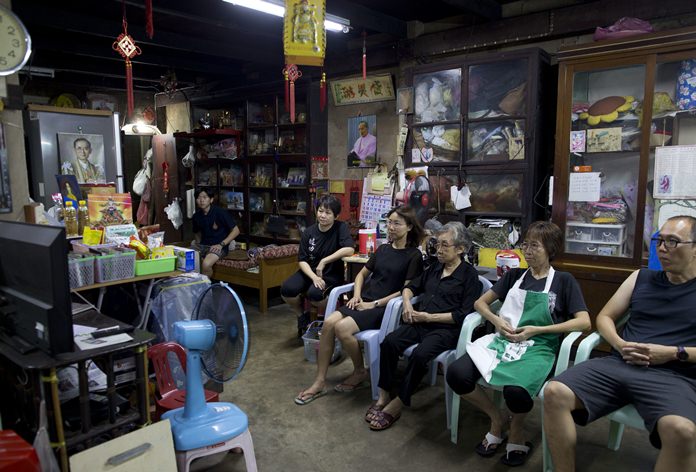 A Thai family sitting in a grocery shop watch a live television broadcast of the funeral of late Thai King Bhumibol Adulyadej in Bangkok, Thursday, Oct. 26, 2017. (AP Photo/Gemunu Amarasinghe)