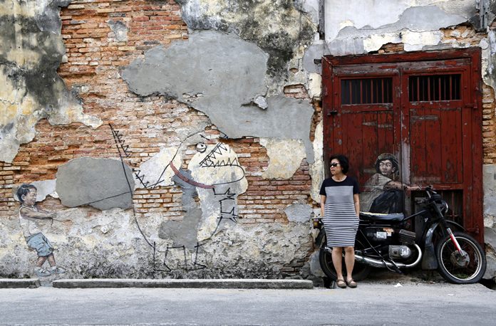 A woman leans against a motorcycle incorporated into a street art installation by artist Ernest Zacharevic in George Town. George Town oozes a hauntingly rustic charm, with colorful street art as much a draw as the historical architecture and one of Southeast Asia’s tastiest street food scenes. (AP Photo/Adam Schreck)
