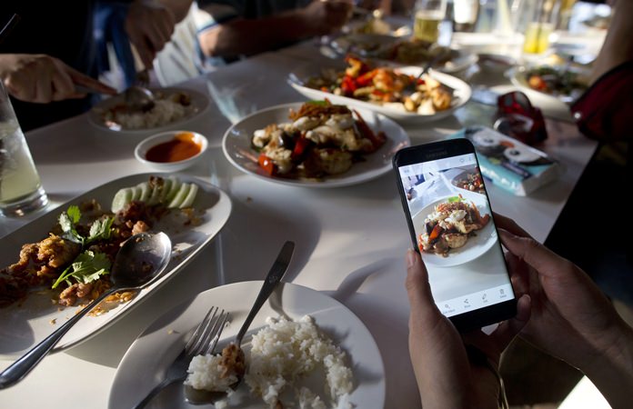 A customer takes photos of food cooked by Thai cook Supinya Jansuta, 72, better known as “Jay Fai,” at her eatery in Bangkok. (AP Photo/Gemunu Amarasinghe)