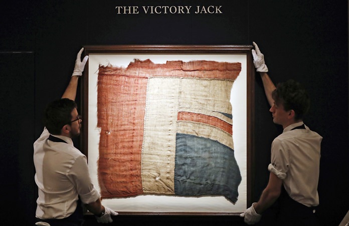 In this Thursday, Jan. 11, 2018 file photo, Sotheby’s employees adjust a frame with a fragment of the Union Flag, which flew from HMS Victory at the Battle of Trafalgar, in London. (AP Photo/Frank Augstein)