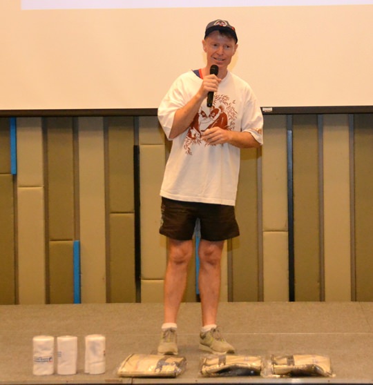 To get things started for learning to be an Aussie for a day, Ren (Lubra Lips) Lexander explains how a little contest between tables involving who can give the Aussie sports call the loudest will win some of the prizes shown at his feet.