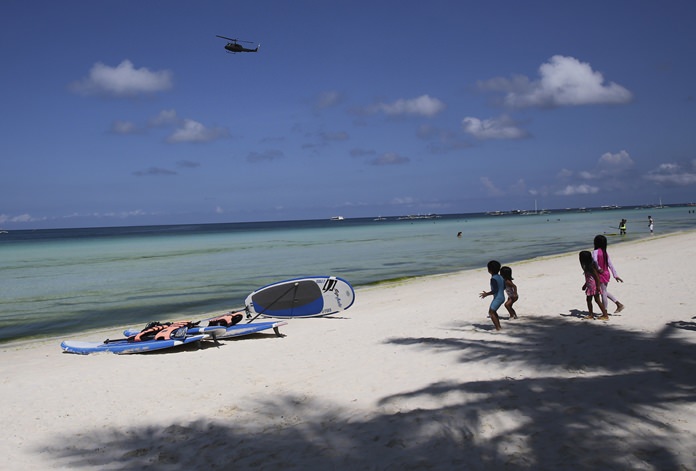 Children watch as a military helicopter passes by the country’s most famous beach resort island Wednesday, April 25, 2018, a day before the government implements its temporary closure. (AP Photo/Aaron Favila)