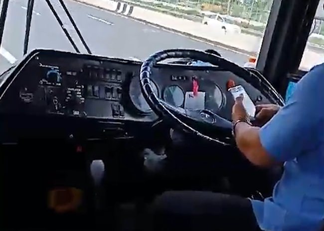 A photo shows the driver using his mobile phone while driving a bus full of passengers.