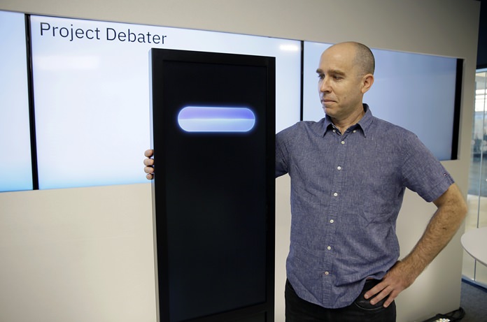 Dr. Noam Slonim, principal investigator, stands with the IBM Project Debater before a debate between the computer and two human debaters Monday, June 18, 2018, in San Francisco. The system, called Project Debater, is designed to be able to listen to an argument, then respond in a natural-sounding way, after pulling in evidence it collects from Wikipedia, journals, newspapers and other sources to make its point. (AP Photo/Eric Risberg)