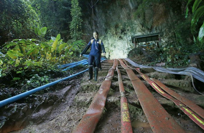 A rescuer makes her way down muddy steps past water pump hoses at the entrance to a cave complex where it's believed that 12 soccer team members and their coach went missing, Friday, June 29, 2018, in Mae Sai, Chiang Rai province, in northern Thailand. (AP Photo/Sakchai Lalit)