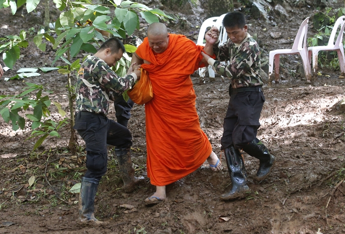A Buddhist monk, helped by Thai rescues, walks after praying near a cave complex where 12 boys and their soccer coach went missing, in Mae Sai, Chiang Rai province, in northern Thailand, Sunday, July 1, 2018. (AP Photo/Sakchai Lalit)