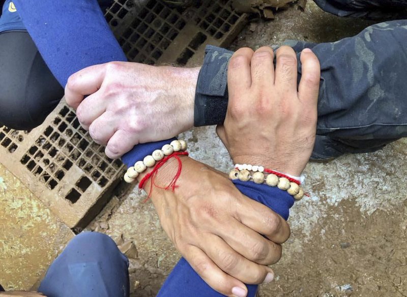 This undated photo released via the Thailand Navy SEAL Facebook page on Sunday, July 8, 2018, shows rescuers hands locked with a caption reading "We Thai and the international teams join forces to bring the young Wild Boars home" where 12 boys and their soccer coach have been trapped since June 23 in a cave in Mae Sai, Chiang Rai province, northern Thailand. The operation has begun to rescue 12 boys and their soccer coach who will need to dive out of the flooded Thai cave where they have been trapped for more than two weeks, with officials saying Sunday morning that "today is D-Day. (Thailand Navy SEAL Facebook page via AP)