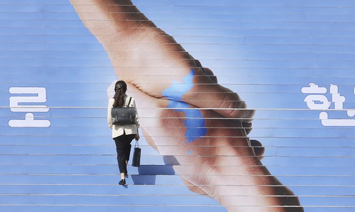 A woman passes by an image of two hands shaking to form the shape of the Korean Peninsula to mark the inter-Korean summit in Seoul, South Korea. (AP Photo/Ahn Young-joon, File)