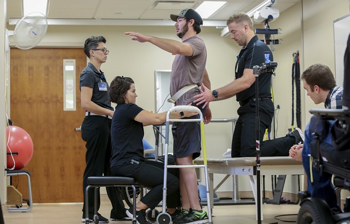 Jered Chinnock stands with the assistance of his therapy team at the Mayo Clinic in Rochester, Minn., on Sept. 18, 2018. Chinnock, paralyzed since 2013, can stand and take steps again thanks to an electrical implant that zaps his injured spine and months of intense rehab as part of a medical study at the clinic. From left are Margaux Linde, Megan Gill, Chinnock, Daniel Veith and Jonathan Calvert. (AP Photo/Teresa Crawford)