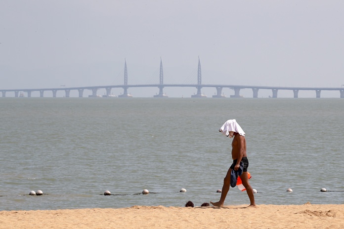 A man walks past a beach as the Zhuhai-Macau-Hong Kong Bridge looms in the background in Zhuhai in south China’s Guangdong province. (AP Photo/Andy Wong)