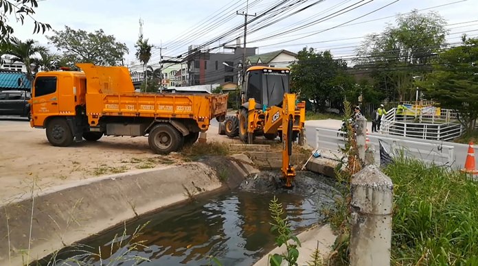 Sanitation workers use a backhoe and dump truck to scoop out natural and man-made debris from the Nongprue 2 Community canal.