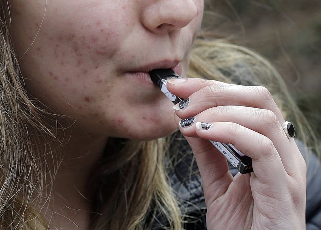 In this April 11, 2018 file photo, a high school student uses a vaping device near a school campus in Cambridge, Mass. (AP Photo/Steven Senne, File)