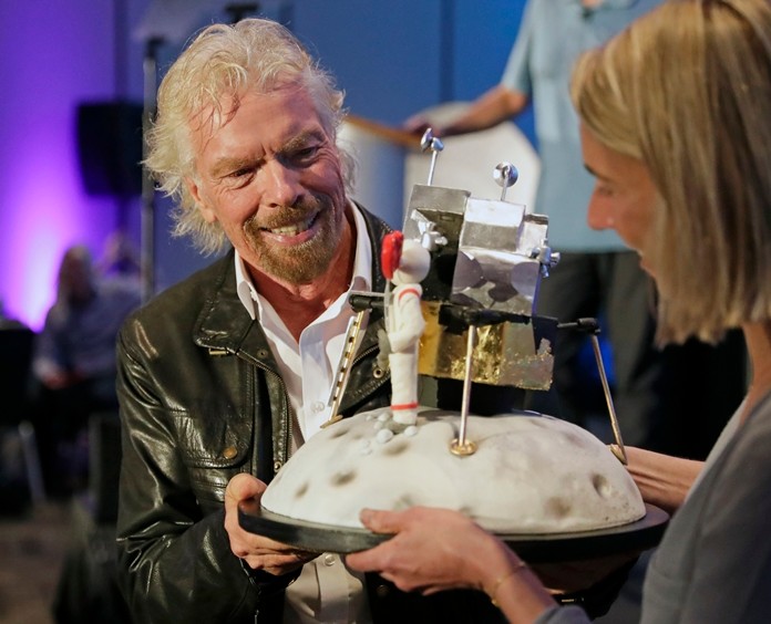 Richard Branson is presented with a space-themed cake during a luncheon attended by 100 Virgin Galactic ticket holders, to mark his 69th birthday and in recognition of the Apollo 11 moon landing anniversary at the Kennedy Space Center Visitor Complex, Thursday, July 18, 2019, in Cape Canaveral, Fla. (AP Photo/John Raoux)