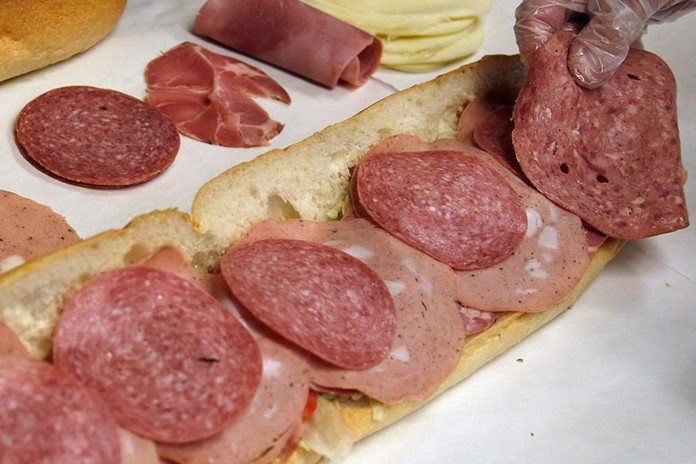 In this June 5, 2014, file photo, a man makes a submarine sandwich with mortadella, cooked salami, ham, Genoa salami and sweet capicola at a delicatessen in Massachusetts. An international team of researchers is questioning the advice to limit red and processed meats, saying the link to cancer and heart disease is weak. (AP Photo/Elise Amendola, File)