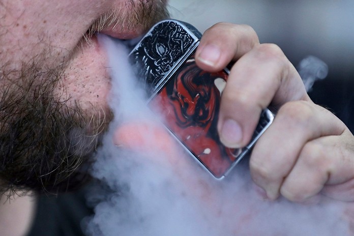 In this Friday, Oct. 4, 2019 photo, a man using an electronic cigarette exhales in Mayfield Heights, Ohio. Vaping-related illnesses in the U.S. are still rising, though at a slightly slower pace. (AP Photo/Tony Dejak)