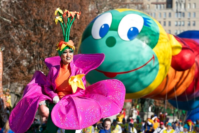 A woman in a flower costume marches in front of the Wiggle Worm balloon during the Macy's Thanksgiving Day Parade, Thursday, Nov. 28, 2019, in New York. (AP Photo/Mark Lennihan)