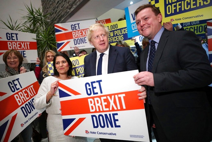 Home Secretary Priti Patel, center left, Britain's Prime Minister Boris Johnson, center, and MP Will Quince pose holding a sign before a rally event as part of the General Election campaign, in Colchester, England, Monday, Dec. 2, 2019. (Hannah McKay/Pool Photo via AP)