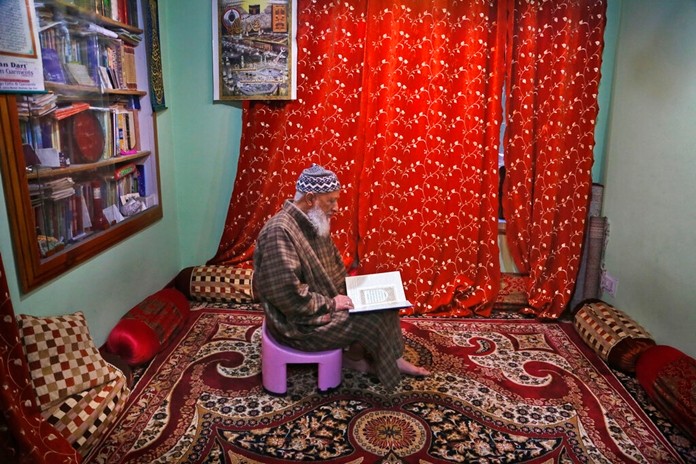 In this Nov. 19, 2019 photo, Mohammed Yasin Bangi, muezzin at grand Jamia Masjid, city's main mosque reads holy Quran inside his home in Srinagar, Indian controlled Kashmir. (AP Photo/Mukhtar Khan)