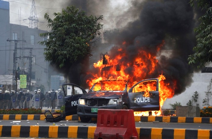 Police officers gather next to a burning police vehicles that were set on fire by angry lawyers during clashes in Lahore, Pakistan, Wednesday, Dec. 11, 2019. (AP Photo/K.M. Chaudary)