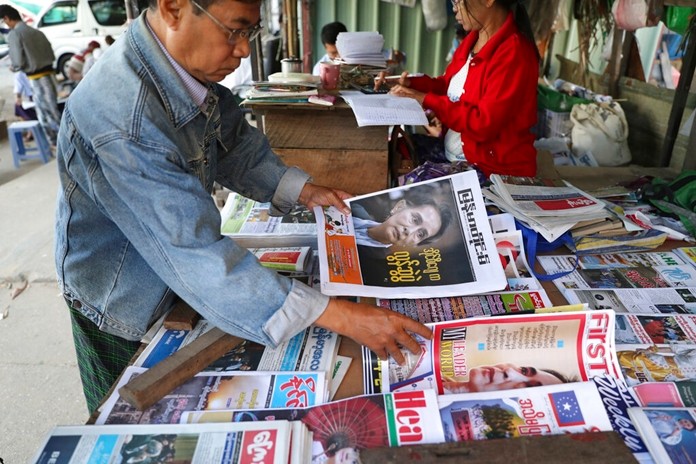 A man looks through newspapers with front pages leading with Myanmar leader Aung San Suu Kyi at the International Court of Justice hearing, near a roadside journal shop Thursday, Dec. 12, 2019, in Yangon, Myanmar. (AP Photo/Thein Zaw)