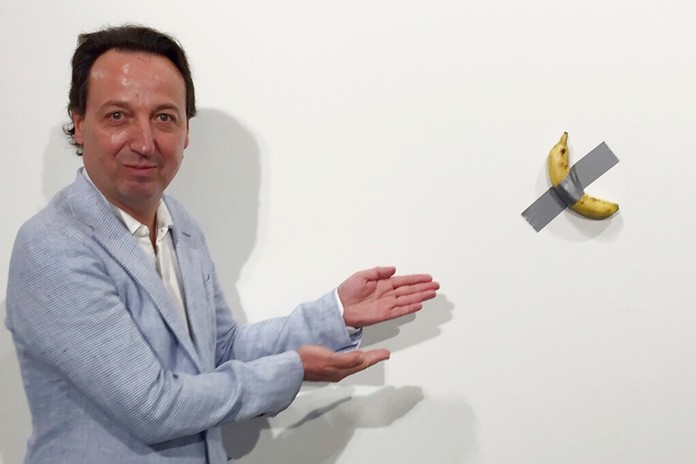 In this Dec. 4, 2019 photo, gallery owner Emmanuel Perrotin poses next to Italian artist Maurizio Cattlelan’s “Comedian” at the Art Basel exhibition in Miami Beach, Fla. The work sold for $120,000. (Siobhan Morrissey via AP)