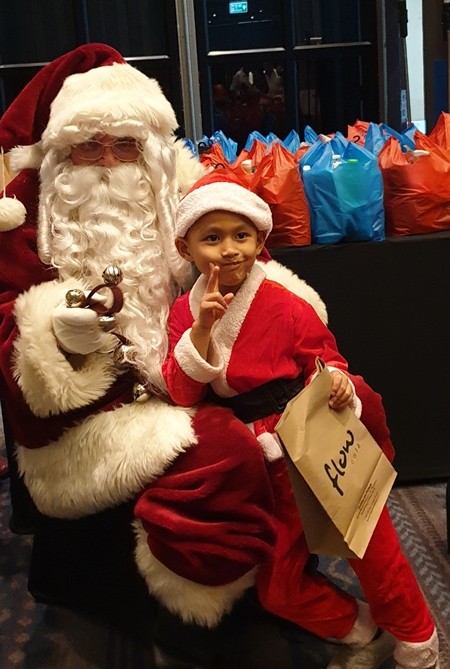 A victory sign is flashed by this young fellow as after he accepts his Christmas Present from Santa.