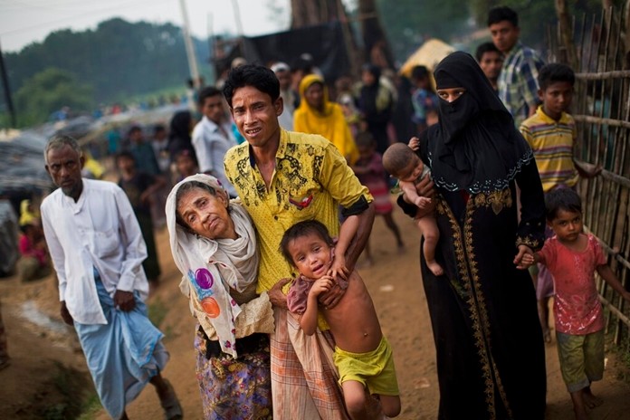In this Sept. 5, 2017, file photo, an exhausted Rohingya helps an elderly family member and a child as they arrive at Kutupalong refugee camp after crossing from Myanmar to the Bangladesh side of the border, in Ukhia. (AP Photo/Bernat Armangue, File)