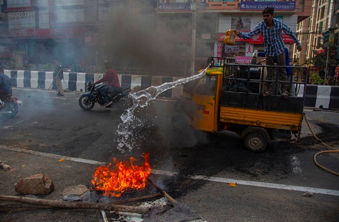 Police clear road blocks as a man tries to douse a fire set by protestors in Gauhati, India, Thursday, Dec. 12, 2019. (AP Photo/Anupam Nath)