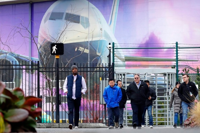 Boeing workers exit the plant in front of a giant mural of a jet on the side of the manufacturing building behind Monday, Dec. 16, 2019, in Renton, Wash. (AP Photo/Elaine Thompson)