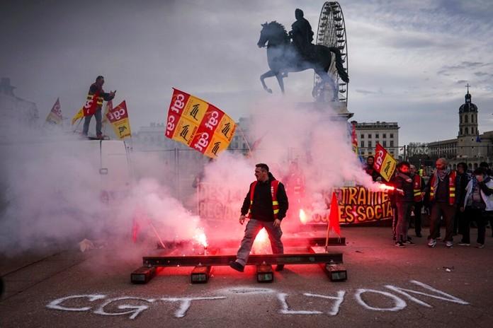 A protester passes by flares during a demonstration in Lyon, central France, Tuesday, Dec. 17, 2019. (AP Photo/Laurent Cipriani)