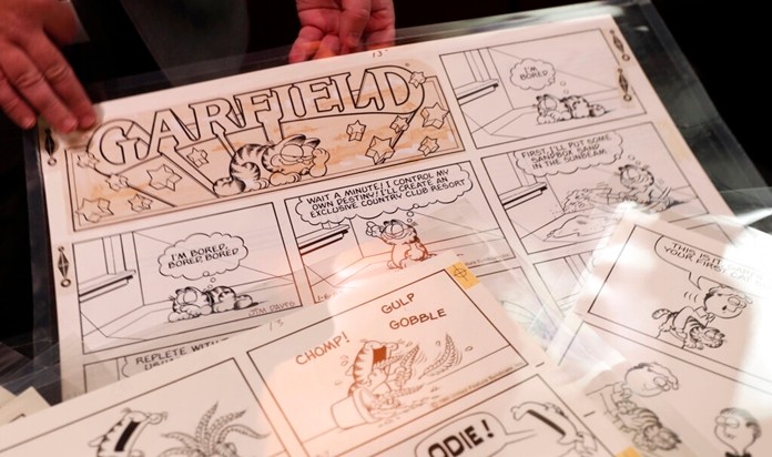 In this Monday, Nov. 18, 2019 photo, Heritage Auctions collectibles specialist Brian Wiedman displays Garfield comic artwork drawn by creator Jim Davis in Dallas. Thousands of the comics drawn by Davis are going up for auction. (AP Photo/LM Otero)