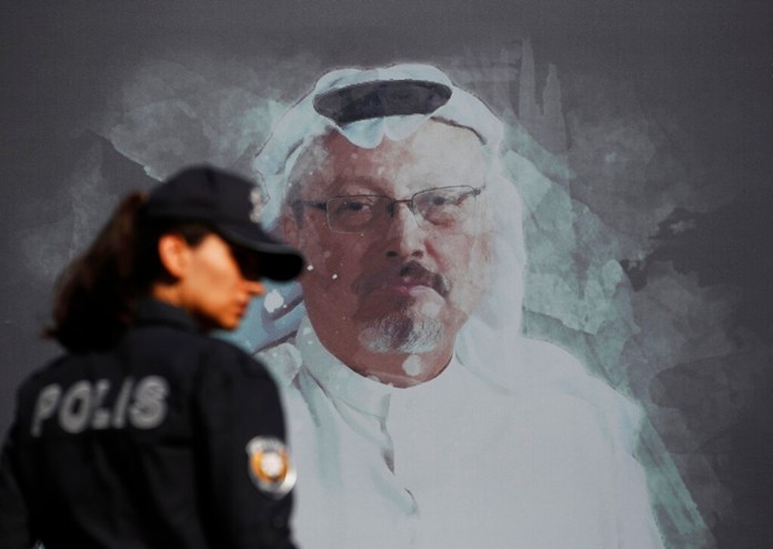 In this Oct. 2, 2019 file photo, a Turkish police officer walks past a picture of slain Saudi journalist Jamal Khashoggi prior to a ceremony, near the Saudi Arabia consulate in Istanbul, marking the one-year anniversary of his death.(AP Photo/LefterisPitarakis, File)