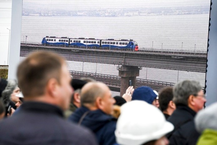 People watch a giant TV screen with Russian President Vladimir Putin, inside, riding a train across a bridge linking Russia and the Crimean peninsula in Taman, Russia, Monday, Dec. 23, 2019. (AP Photo)