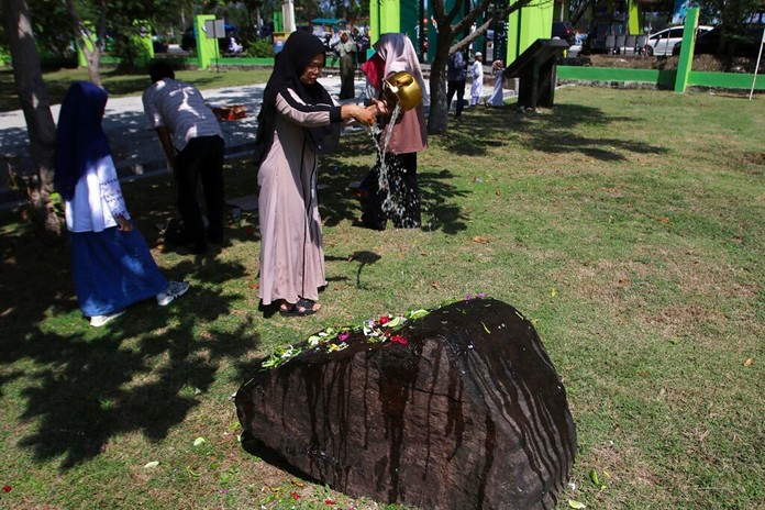 A woman pours water at a stone marking the mass grave for the victims of the Indian Ocean tsunami following prayers commemorating the 15th anniversary of the disaster in Banda Aceh, Indonesia, Thursday, Dec. 26, 2019. (AP Photo/Nurhasanah)
