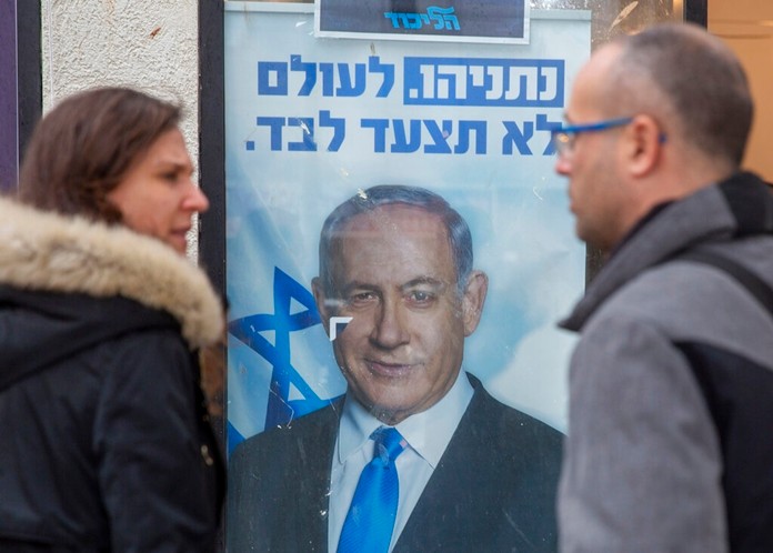 People look at a poster of Israel Prime Minister and governing Likud party leader Benjamin Netanyahu at a voting center in the northern Israeli city of Hadera, Thursday, Dec. 26, 2019 (AP Photo/Ariel Schalit)