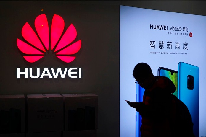 In this Dec. 11, 2018, photo, a man browses his smartphone outside a Huawei store at a shopping mall in Beijing. (AP Photo/Andy Wong)