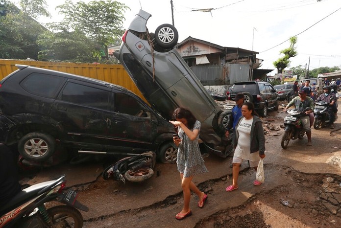 Residents walk near the wreckage of cars that were swept away by flood in Bekasi, West Java, Indonesia, Friday, Jan. 3, 2020. (AP Photo/Achmad Ibrahim)