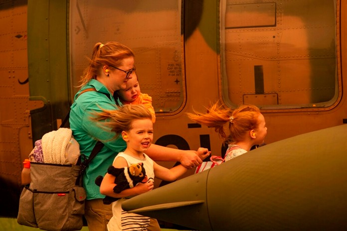 In this Jan. 4, 2020 photo provided by the Australian Department of Defence, a woman and three children prepare to board an Australian Army Blackhawk helicopter in Omeo, Victoria, Australia, for evacuation from the wildfire effected area. The wildfires have so far scorched an area twice the size of the U.S. state of Maryland. (Corporal Nicole Dorrett/ADF via AP)