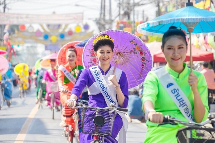 Parade of ladies riding bicycles and holding umbrellas.
